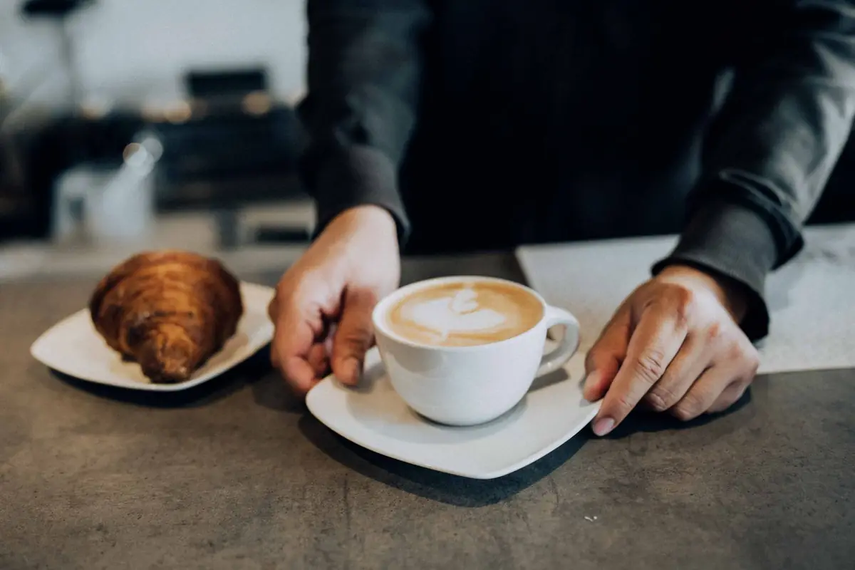 A cappuccino and a croissant handed across the counter